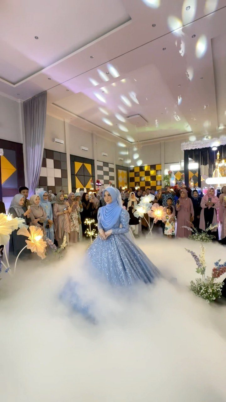 Woman in a sparkling light blue wedding gown and hijab standing in white fog