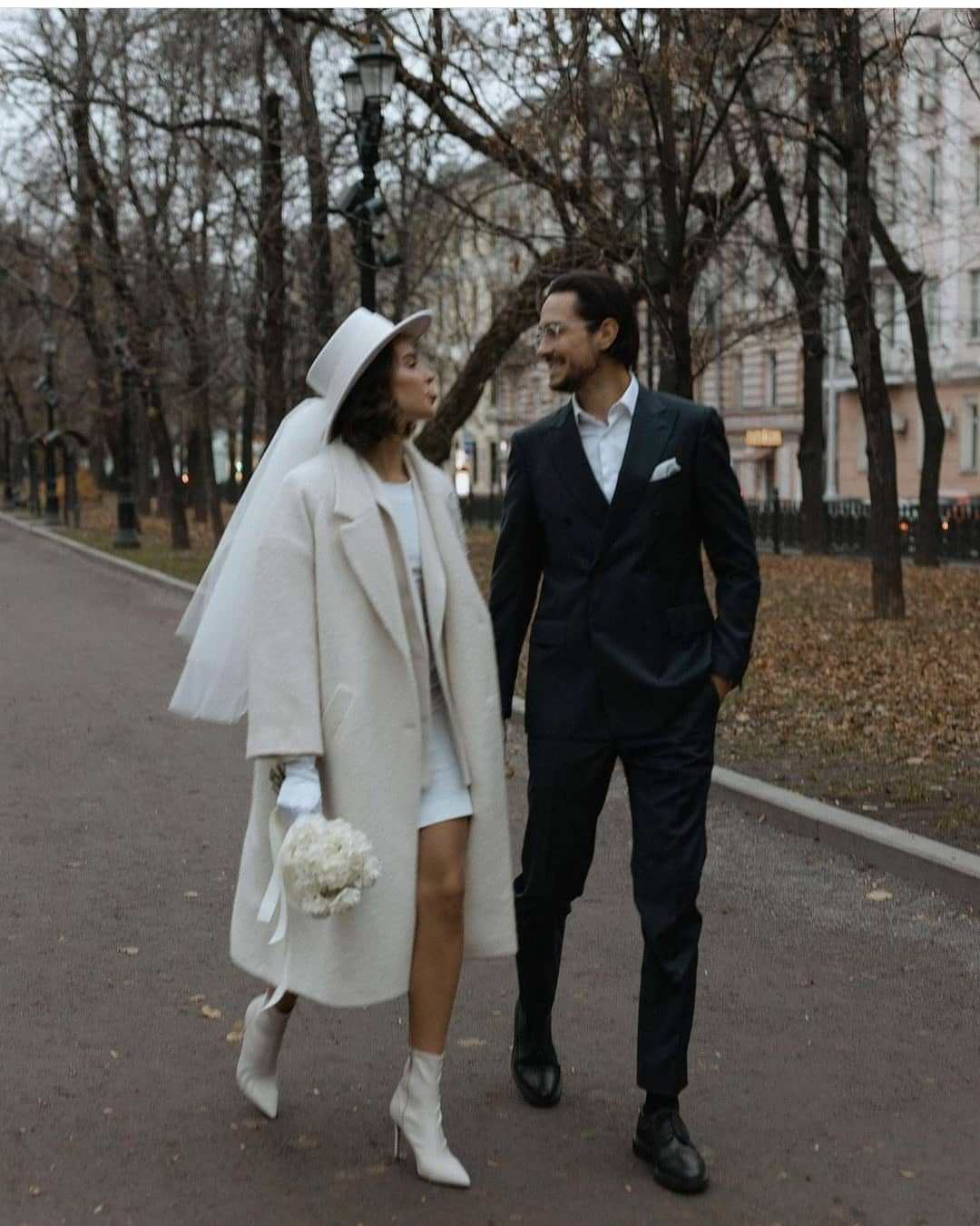 Bride in white coat and ankle boots walking with groom in dark suit.